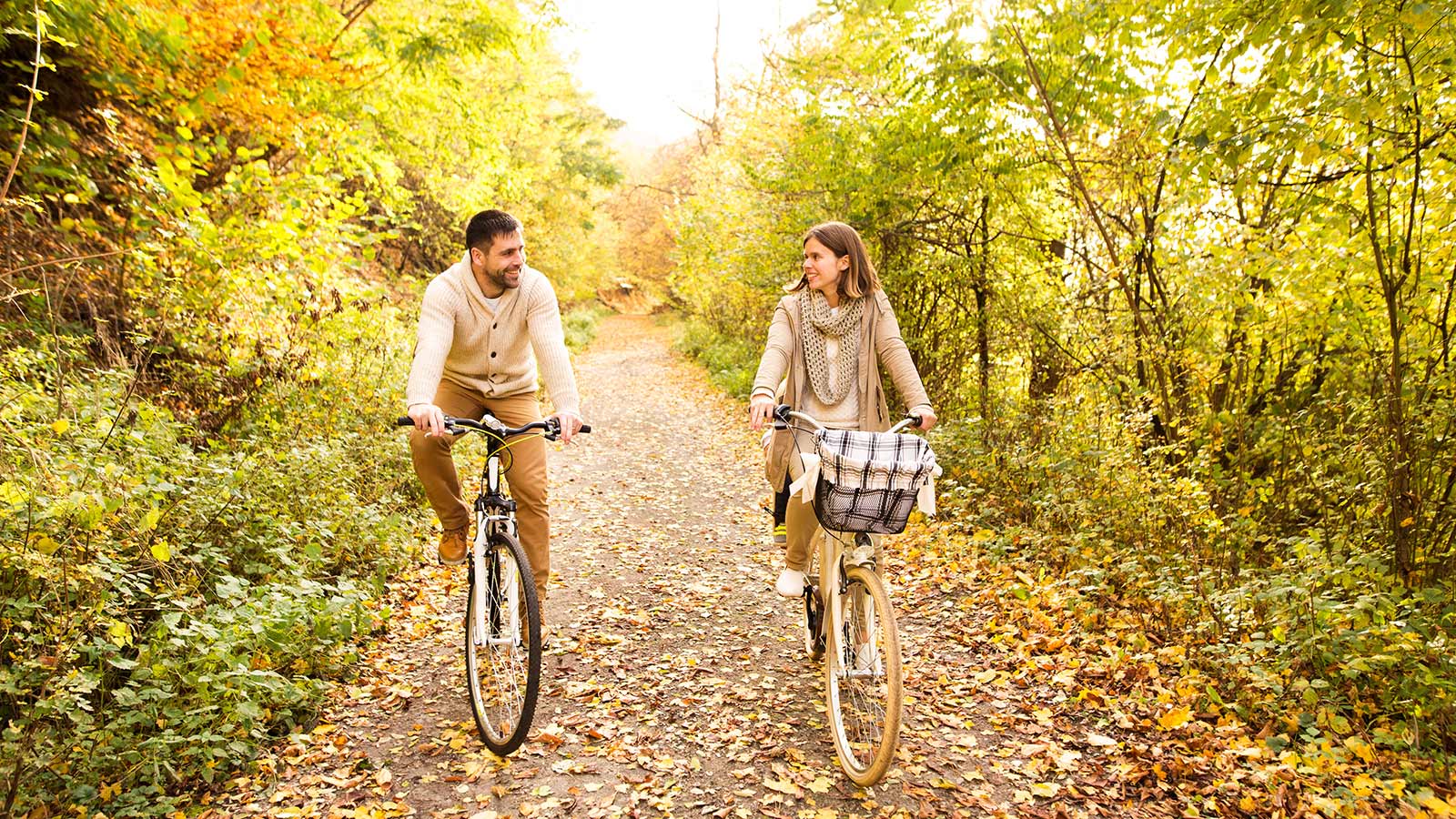Man and woman cycling down a pathway covered in fall leaves