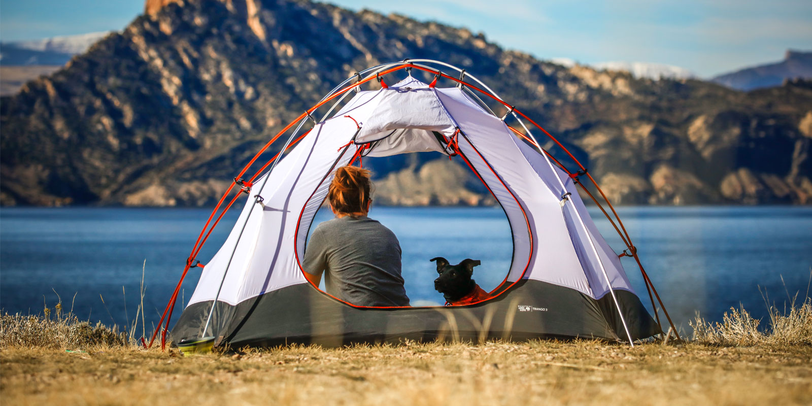 Woman sitting open sided dome tent with black dog looking over a lake
