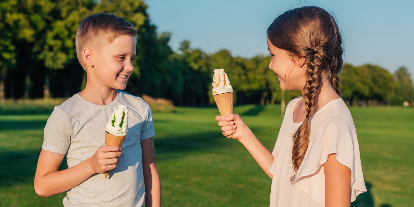 Two smiling children eating ice cream at a park.