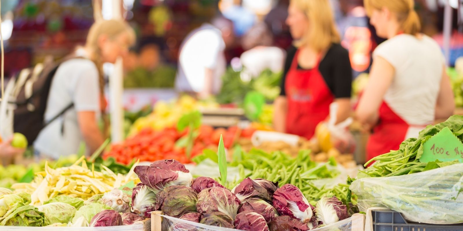 Close up shot of vegetables at a farmer's market table with customers in background.